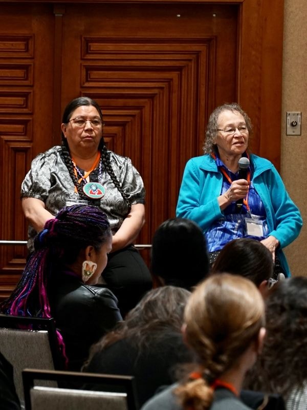 Two women speaking to an audience at an indoor event